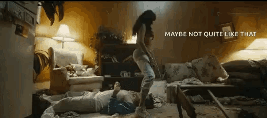 a woman is standing on top of a man laying on the floor in a messy living room .