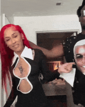 a woman with red hair is standing next to a man wearing sunglasses and a black dress .