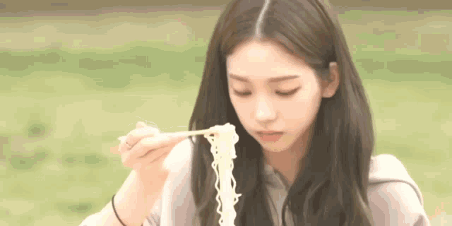 a young woman is eating noodles with chopsticks in a park .