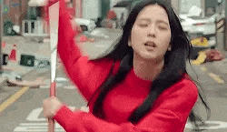 a woman in a red sweater is holding a knife in her hand while standing on a street .
