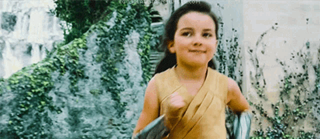 a little girl in a yellow dress is running in front of a waterfall