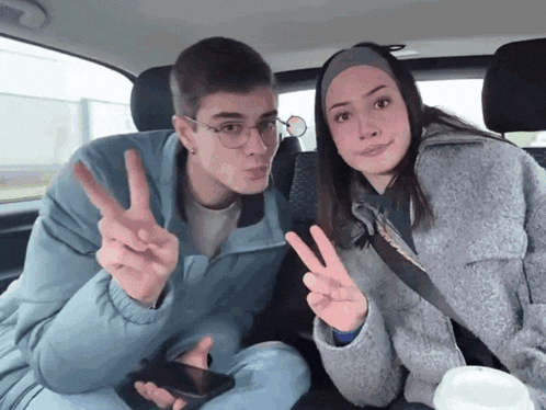 a man and a woman are sitting in a car giving a peace sign