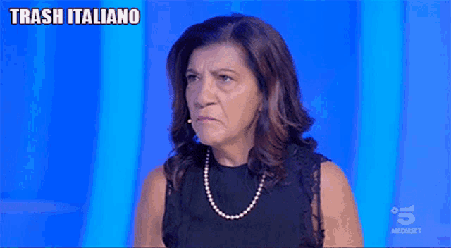a woman wearing a black top and a pearl necklace says trash italiano on the bottom of her face