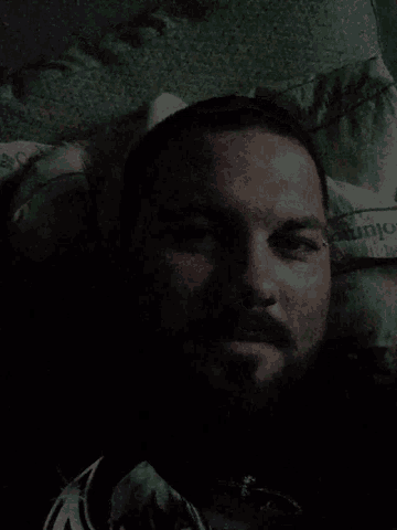 a man with a beard is laying on a bed with a pillow that says columbia on it