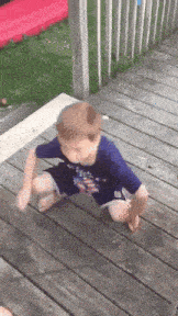 a young boy is squatting on a wooden deck wearing a shirt that says ' united states ' on it
