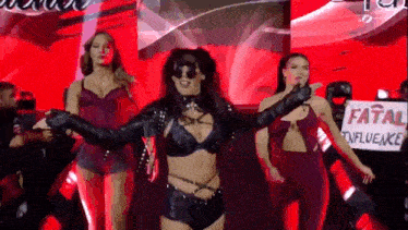 a group of women are dancing on a stage with a sign that says fatal influence on it .