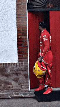 a man in a red suit is standing in front of a red door carrying a helmet .