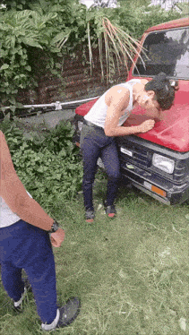 a man in a white tank top is leaning on a red car with a license plate that says ' toyota '