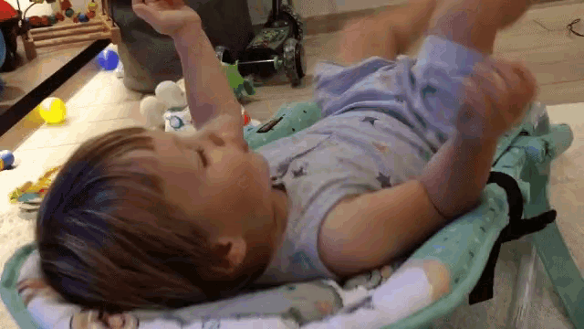 a baby is laying in a bouncer and playing with a toy .