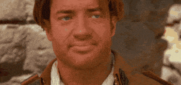 a close up of a man 's face with a stone wall behind him