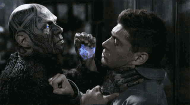 a man with a tattoo on his face holds another man 's hand