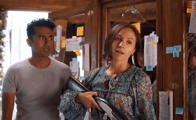a man and a woman are standing next to each other in a room . the woman is holding a gun .