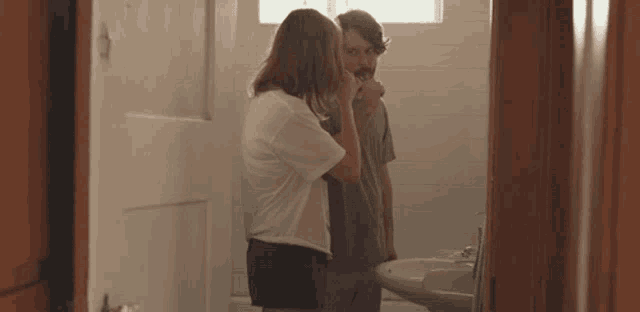 a woman brushes a man 's teeth in the bathroom