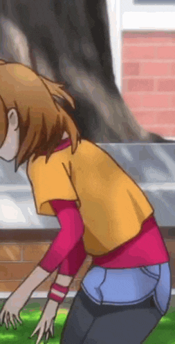 a girl in a yellow shirt and blue jeans is bending over in front of a brick wall .