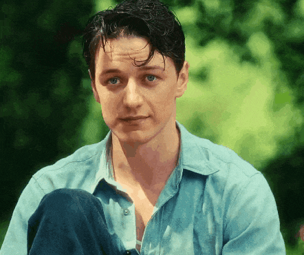 a man in a blue shirt sits with his legs crossed and looks at the camera