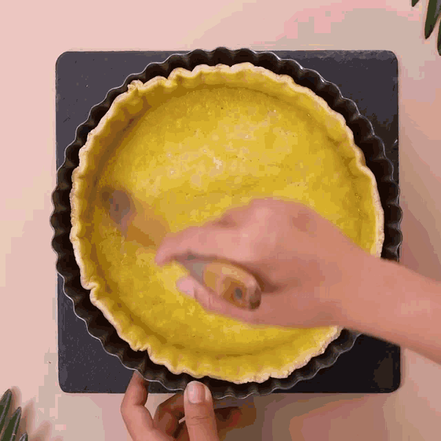 a person is spreading a yellow crust on a pie