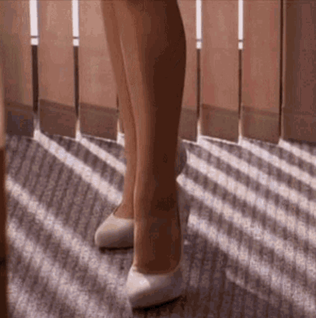 a woman is wearing white high heels and standing on a carpet .