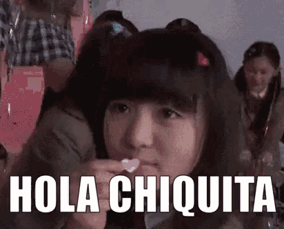 a girl is eating a heart shaped candy and says hola chiquita in spanish .