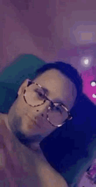 a man wearing glasses is laying on a couch and smiling .
