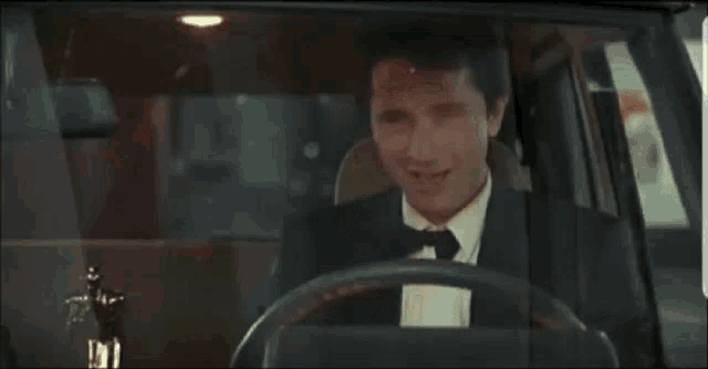 a man in a suit and tie laughs while driving a car