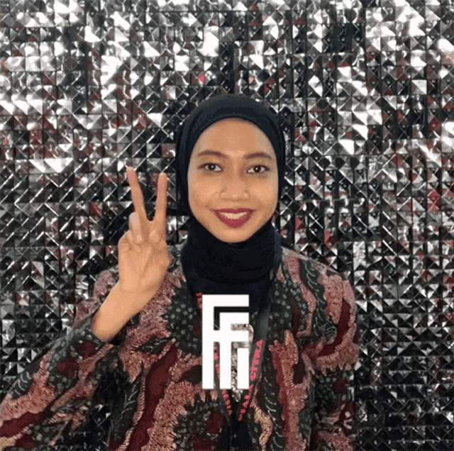 a woman wearing a hijab and a lanyard with the letter f on it giving a peace sign
