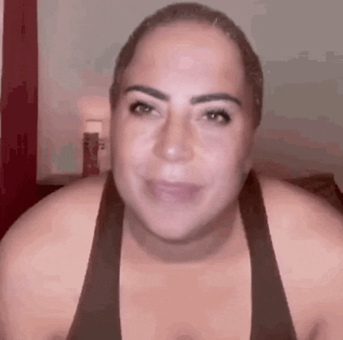 a woman with a shaved head is smiling and looking at the camera while wearing a black tank top .