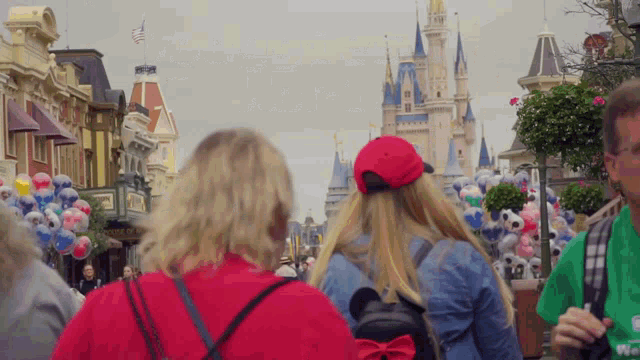 a woman wearing a red hat and a mickey mouse backpack stands in front of a castle