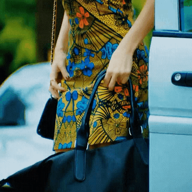 a woman in a colorful dress is holding a black bag