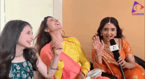 a group of three women are sitting next to each other laughing and holding microphones .