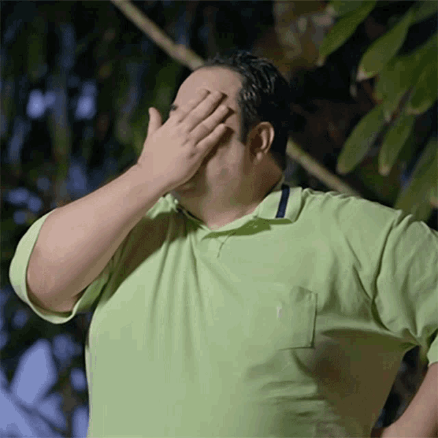 a man in a green polo shirt covering his face