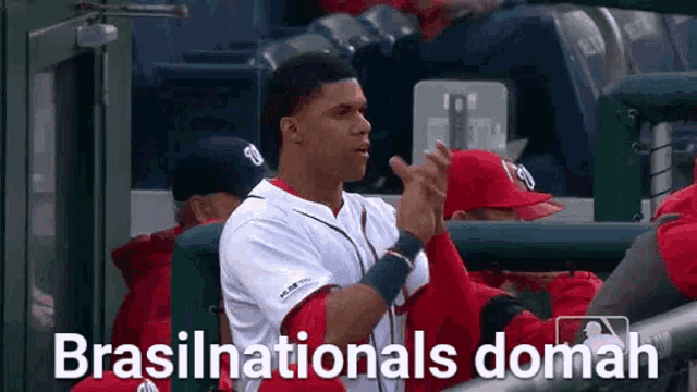 a baseball player is sitting in the dugout applauding his team mates .