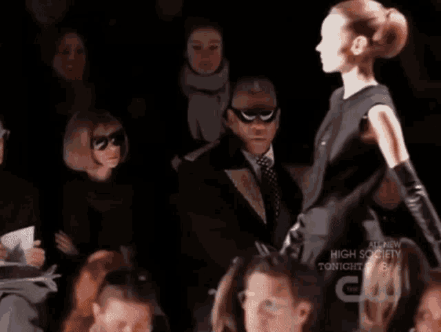 a man in a suit and tie watches a model walk down the runway at a high society fashion show