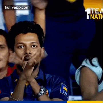 a man in a blue shirt is clapping his hands in the stands .