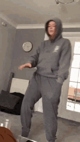 a woman in a hoodie and sweatpants is dancing in a living room