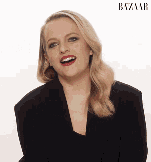 a woman in a black jacket is smiling in front of a white background with the word bazaar on it