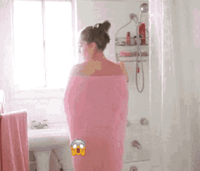 a woman wrapped in a pink towel is standing in the shower .