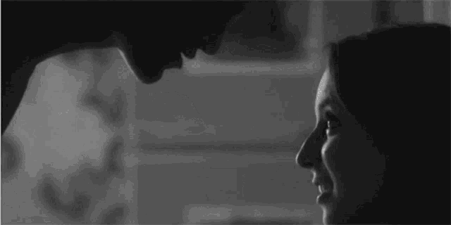 a black and white photo of a man and a woman looking into each other 's eyes .