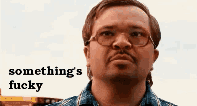 a man wearing glasses and a plaid shirt is looking at the camera with the words `` something 's fucky '' above him .