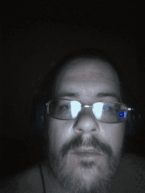 a man with a beard wearing glasses and headphones looks at the camera
