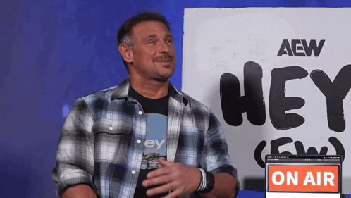 a man in a plaid shirt is standing in front of a sign that says hey
