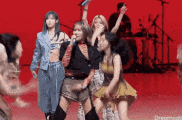 a group of women are dancing and singing on a stage with a red background and the words dreamcat on the bottom right