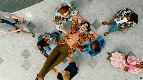a group of people are standing around a shirtless man laying on the floor
