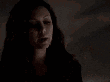 a woman in a black dress is standing in a dark room with a broom .