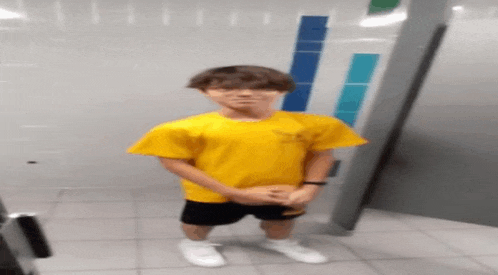 a boy wearing a yellow shirt and shorts is standing in a bathroom .