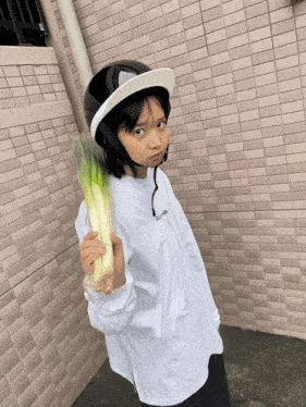 a young girl wearing a helmet and holding a bunch of green onions