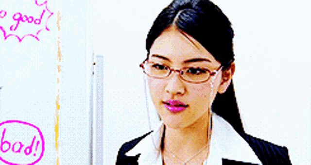 a woman wearing glasses wipes her face in front of a white board that says good bad