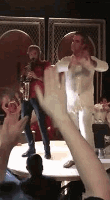 a man is playing a saxophone on a stage while another man stands behind him .