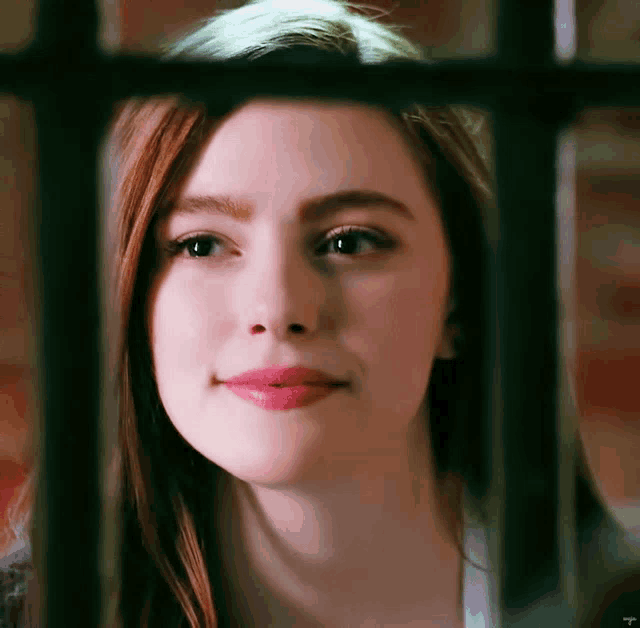 a close up of a woman 's face behind bars with the letter t visible