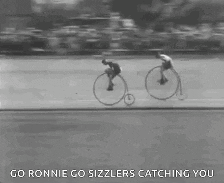 a black and white photo of two men riding bicycles on a road .
