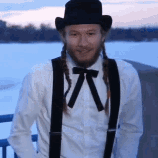 a man wearing a top hat and suspenders stands in front of a body of water